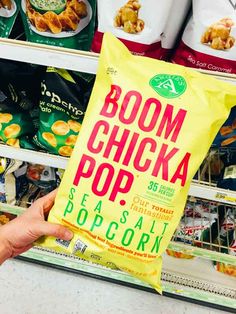 a person holding up a bag of boom chick pop in front of some other snacks