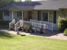 a house with white railings and flower pots on the front porch, next to a lawn