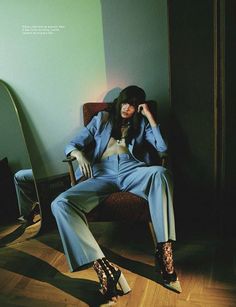 a woman sitting on top of a chair in a blue suit and leopard print boots