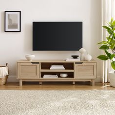 a flat screen tv sitting on top of a wooden entertainment center next to a potted plant