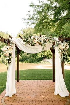 an outdoor wedding ceremony setup with white and pink flowers on the arch, greenery and brick walkway