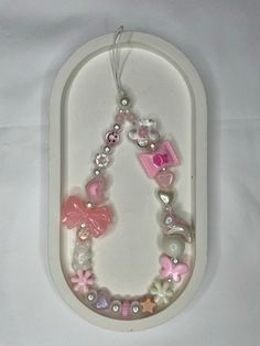 a pink and white beaded necklace with charms on it's side hanging from a hook