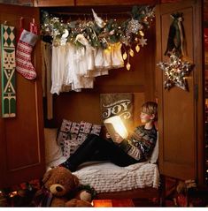 a person sitting on a bed reading a book with christmas lights hanging from the ceiling