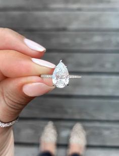 a woman's hand holding a ring with a pear shaped diamond in the middle