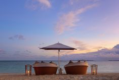 two boats are sitting on the beach under an umbrella at sunset with candles in front of them