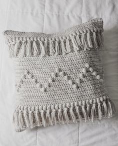 a crocheted pillow with tassels on top of a white bed spread