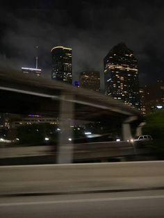 the city skyline is lit up at night as seen from an overpass in this blurry photo