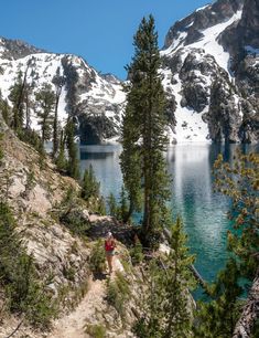 two people hiking up the side of a mountain next to a lake and snow covered mountains