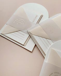 some white envelopes with gold foil on them are laying next to each other in front of a pink background