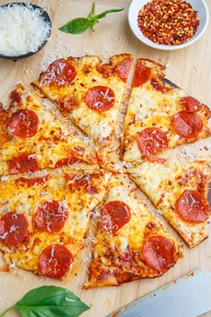 a pizza with pepperoni and cheese on a wooden cutting board next to some seasoning