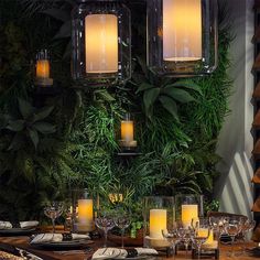 a dining room table with candles and place settings on it, surrounded by greenery