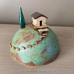 a small house sitting on top of a teal colored pot with a green handle