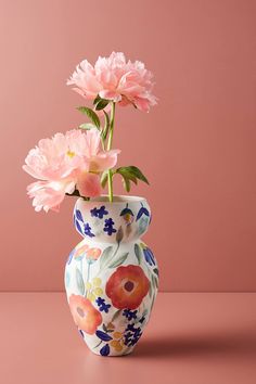 two pink flowers are in a vase on a table against a pink background with the same color as the wall