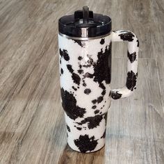 a black and white coffee mug on a wood floor with the lid up to it's side