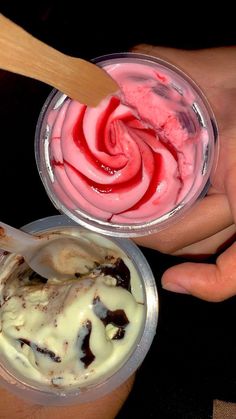 two people are holding ice cream and spoons with red swirl in them on a black table