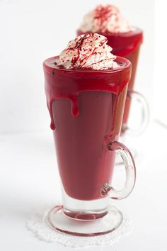 two glasses filled with red liquid and whipped cream