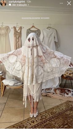 a woman is standing in front of dresses and veils that are hung on the wall