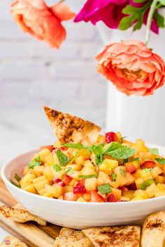 a white bowl filled with fruit salad next to pita wedges and pink flowers