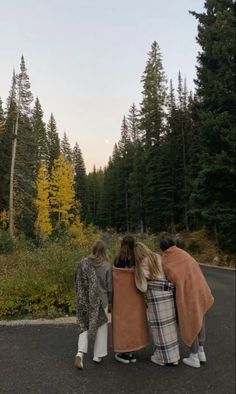 three people standing on the road with their backs to each other and looking at trees