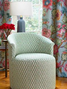 a green chair sitting in front of a window next to a vase with flowers on it