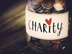 a jar filled with lots of coins sitting on top of a wooden table next to a sign that says charity