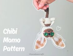 a hand holding a crocheted stuffed animal hanging from a string with the words chibi momo pattern on it