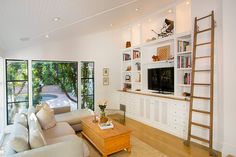 a living room filled with furniture and a tv on top of a wooden shelf next to a window