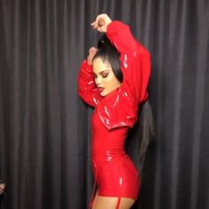 a woman in a red latex outfit posing for the camera with her hands behind her head