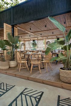 an outdoor dining area with wooden tables and chairs surrounded by potted plants on the deck