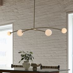 a dining room table with four lights hanging from it's center point and a potted plant in the middle