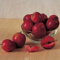 a glass bowl filled with red apples on top of a wooden table