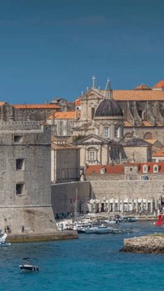 boats are in the water next to an old city with stone walls and orange roofs