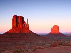 the desert is full of red rocks and tall mountains at sunset or sunrise, as seen from mittens point in monument national park