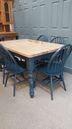 a wooden table with six blue chairs around it in a room that has a gray paneled wall behind it