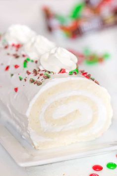 a white plate topped with a roll covered in frosting and sprinkles