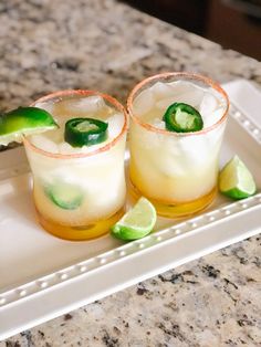 two glasses filled with drinks sitting on top of a white tray next to limes