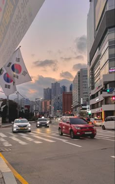 cars are driving down the street in front of tall buildings and skyscrapers at dusk