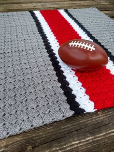 a football is laying on top of a crocheted rug with a red, white and black stripe