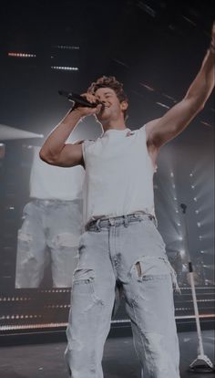 a male in a white shirt and jeans on stage with his hands up to the air