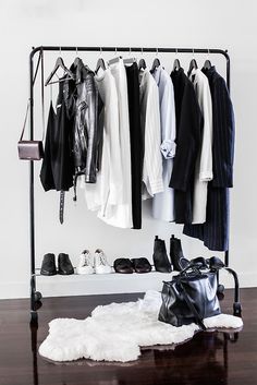 a clothes rack with shoes and bags on it, next to a white rug in front of a wall