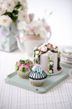 three cupcakes sitting on a tray with flowers in the back ground and two vases behind them