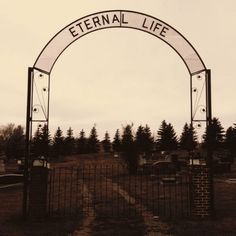 an old photo of a gated entrance to a cemetery with cars parked in the background