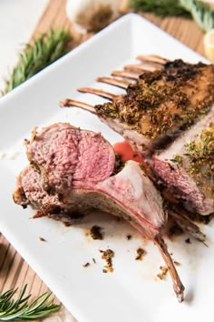 two pieces of meat sitting on top of a white plate next to lemon wedges