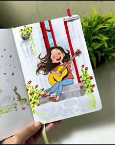 a hand holding an open notebook with a drawing of a girl playing the guitar