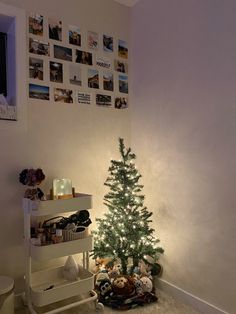 a small christmas tree sitting in the corner of a room with pictures on the wall