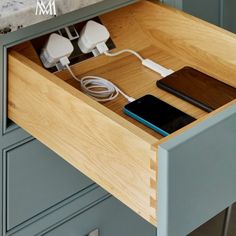 an open drawer in a kitchen with two phones and charger plugged into it