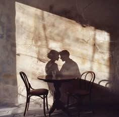 the shadow of two people sitting at a table in front of a stone wall and chair