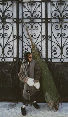 a woman is carrying a tree in front of an iron gate on a snowy day