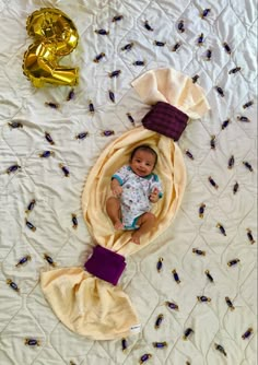 a baby laying on top of a white bed next to gold balloons and streamers