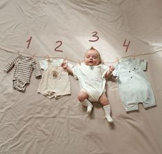 a baby laying on top of a bed next to three ones hanging from clothes line